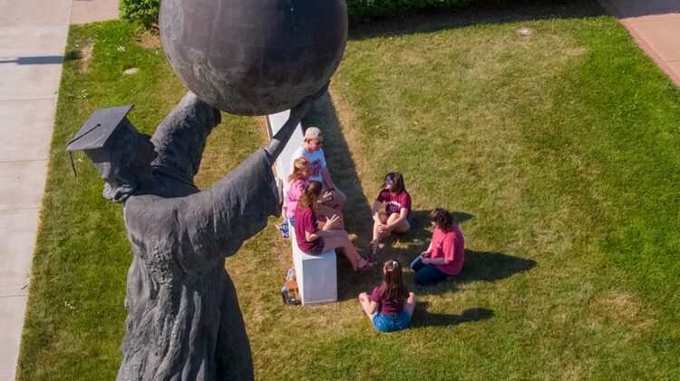 Statue of scholar holding globe with students underneath