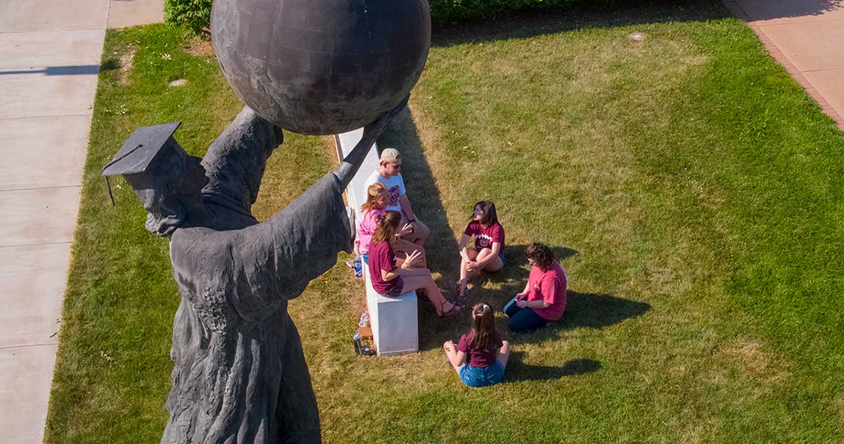 Statue of scholar holding globe with students underneath