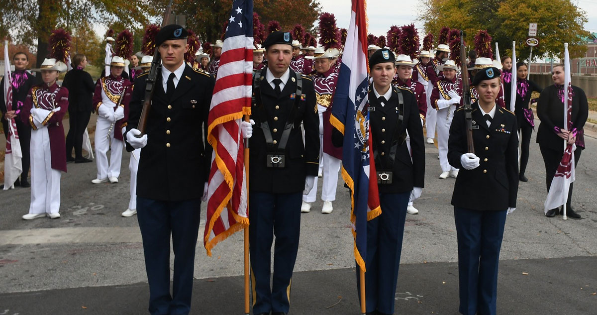 Four military individuals leading parade as color guard