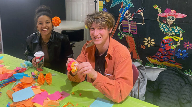 Two student volunteers sit at table with colorful paper