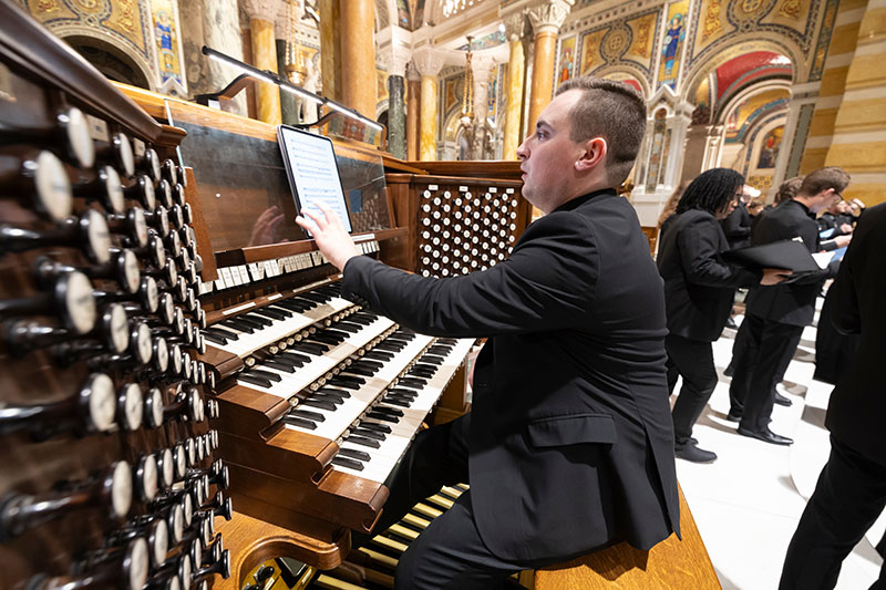 Man in black suit at organ views music notes