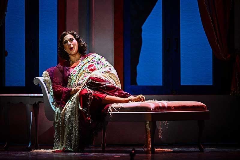 Opera performer lying on couch on stage.
