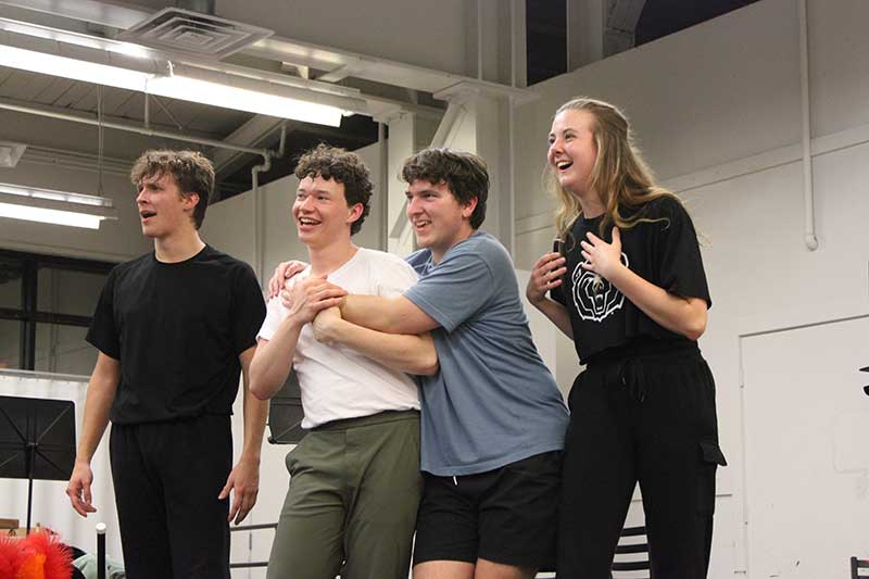 Three young men and one young woman laughing during rehearsal