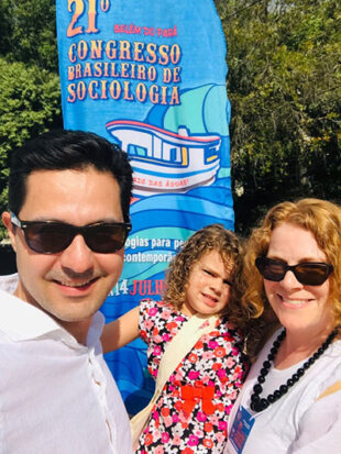 Man, woman and child in sunshine standing next to banner
