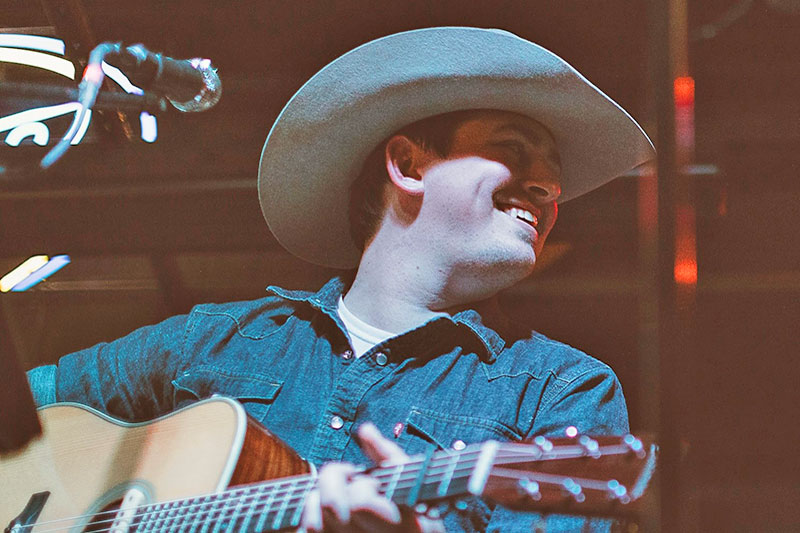 Young man in western clothing with guitar on stage