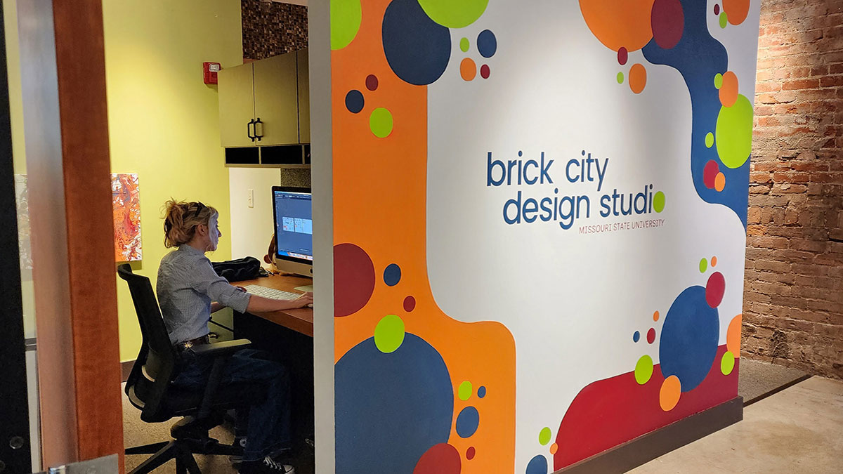 Young person working on a computer behind a colorful wall