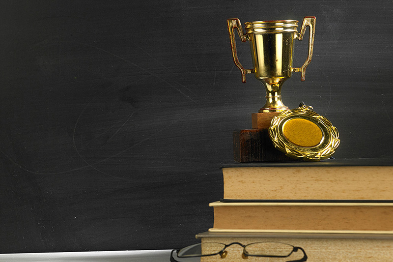 Trophy on top of stack of books in front of blackboard
