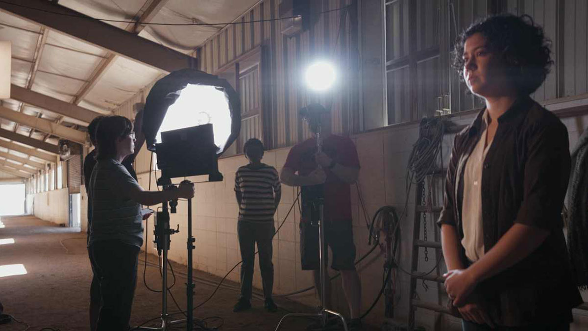 Woman with lighting crew on set in darkened horse stables.