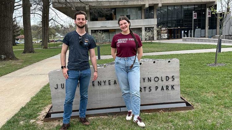 Young man and young woman standing outside near arts park sign