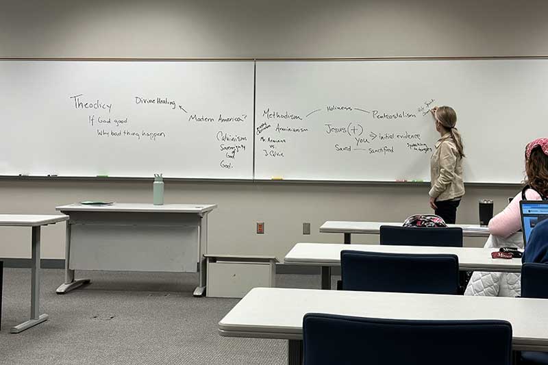 Woman standing in front of classroom writing on board