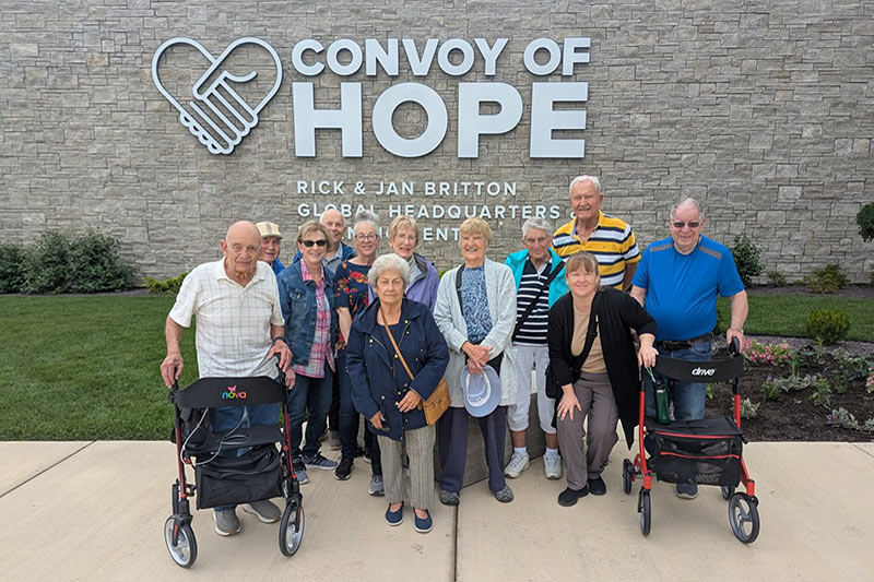 Group of aged persons with their caregiver standing outside a building