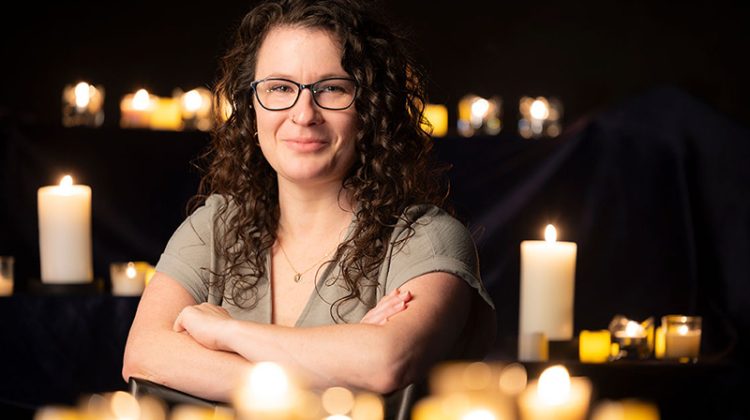 Dr. Erin Wehrman, an associate professor at Missouri State, crosses her arms while posing, surrounded by candles.