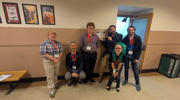 Six individuals casually posing for camera in a hallway