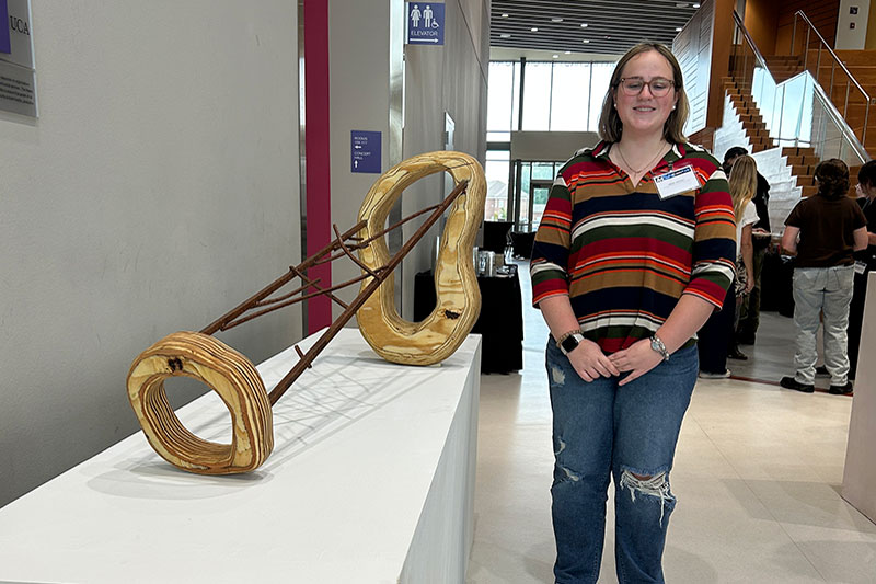 Young woman stands next to sculpture at exhibition