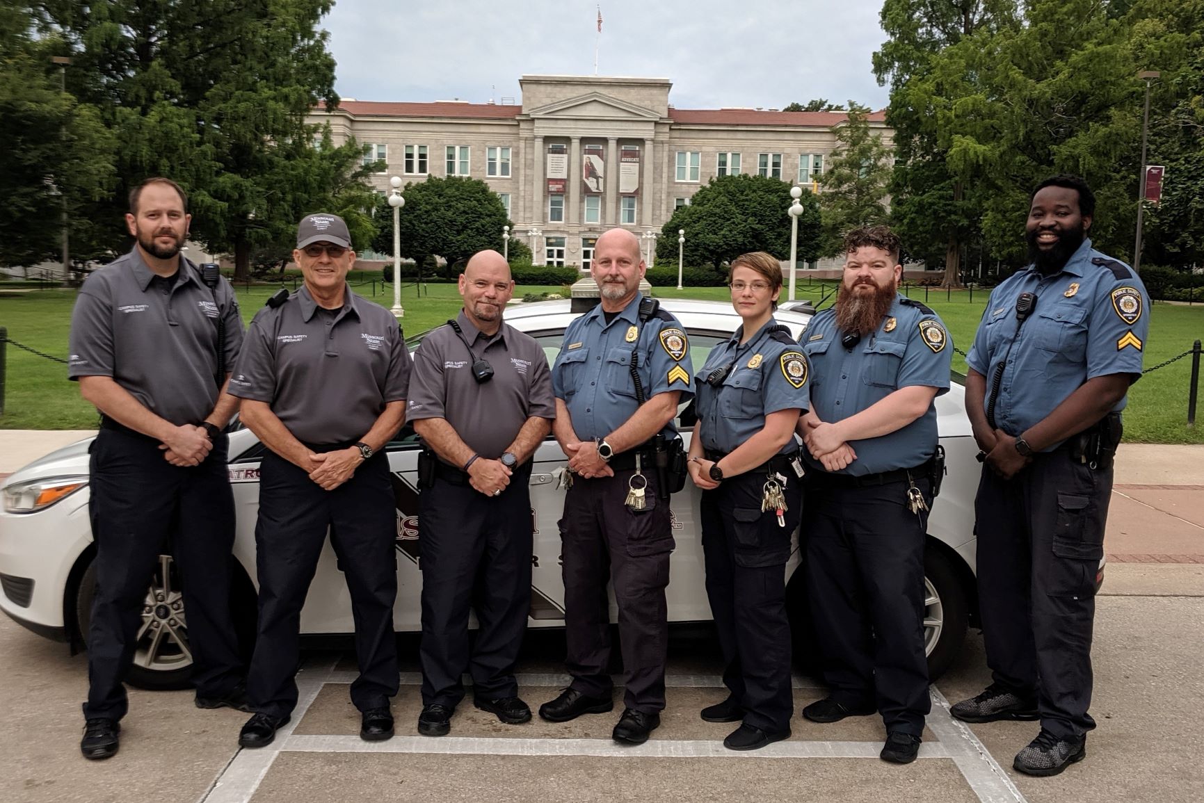 This photo shows the four off-going Campus Safety personnel with the original police style uniform next to the three on-coming personnel with the new polo style uniform.