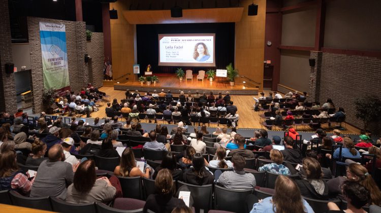 A crowded theater listens to a speaker on stage