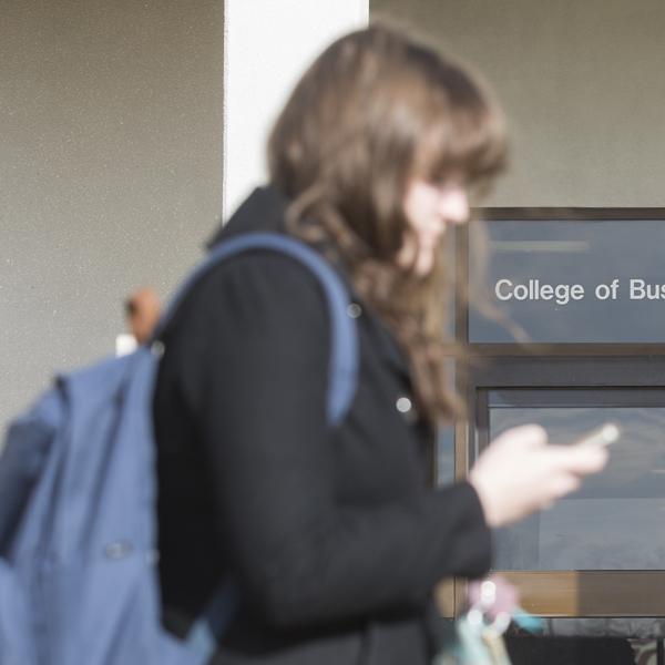 Student reading smartphone outside Colllege of Business
